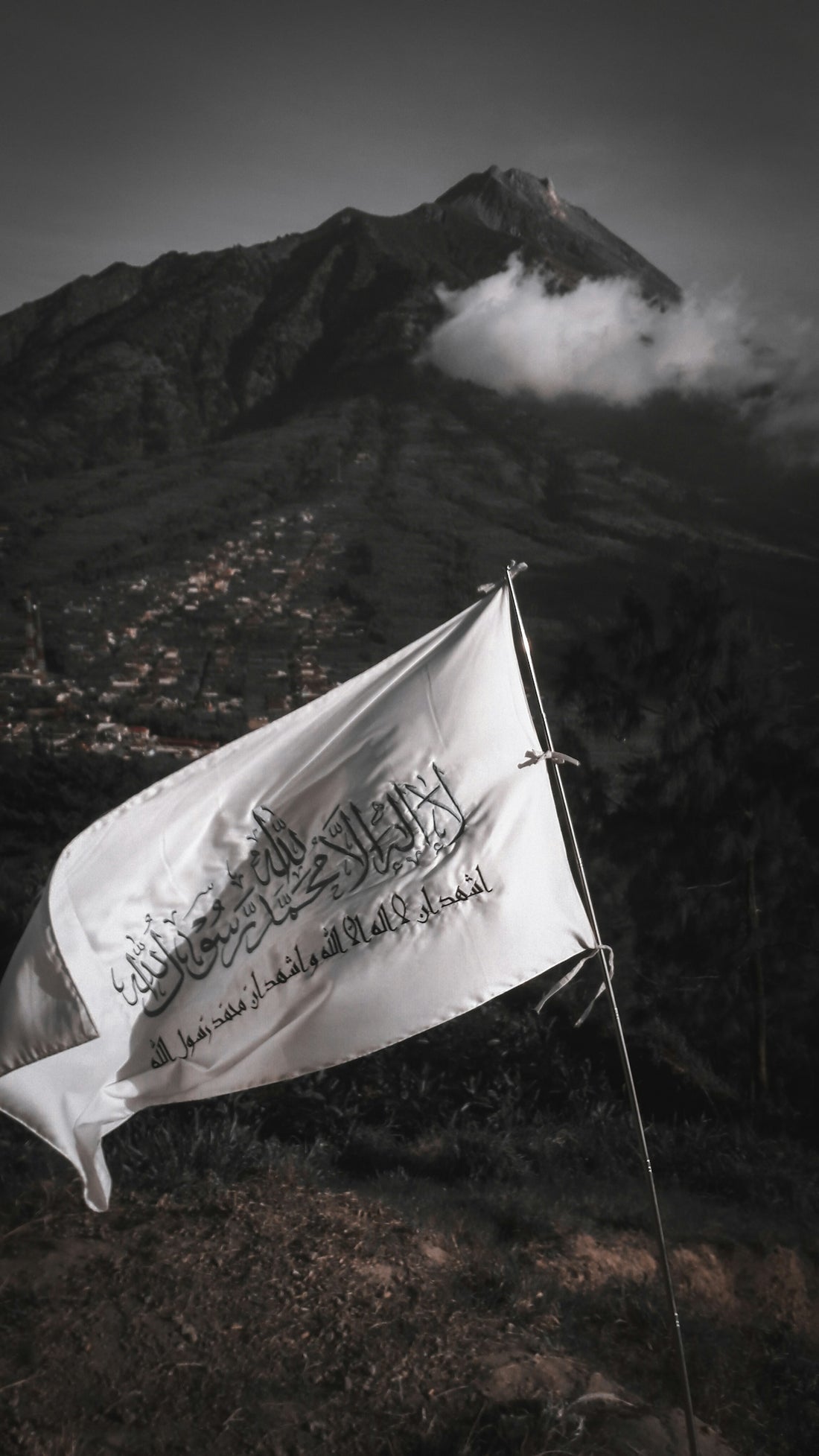 A white flag with black Arabic calligraphy waving before Mount Merbabu in Indonesia