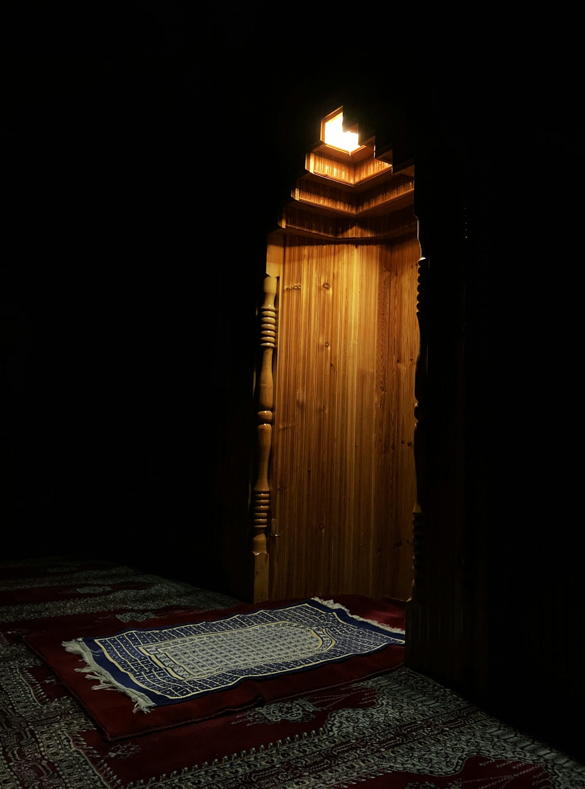 A prayer rug on a red carpet before a wooden mihrab niche