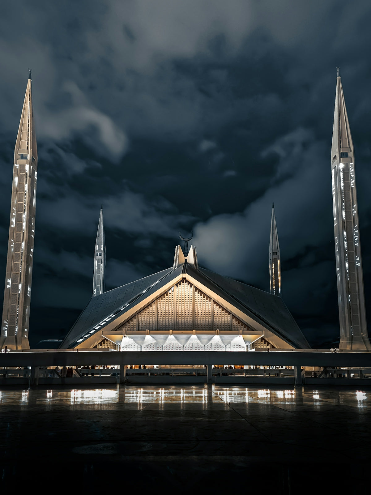 The Shah Faisal Mosque illuminated at night under a cloudy sky in Islamabad